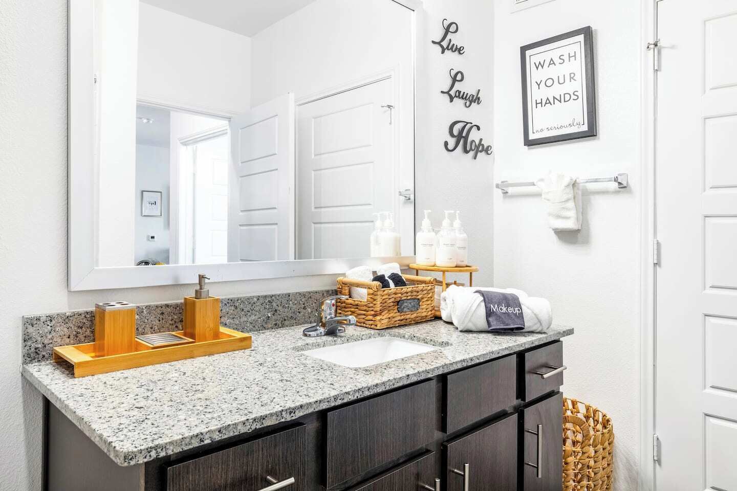 A bathroom with a granite countertop, dark wooden cabinets, a large mirror, and a wall-mounted vanity.