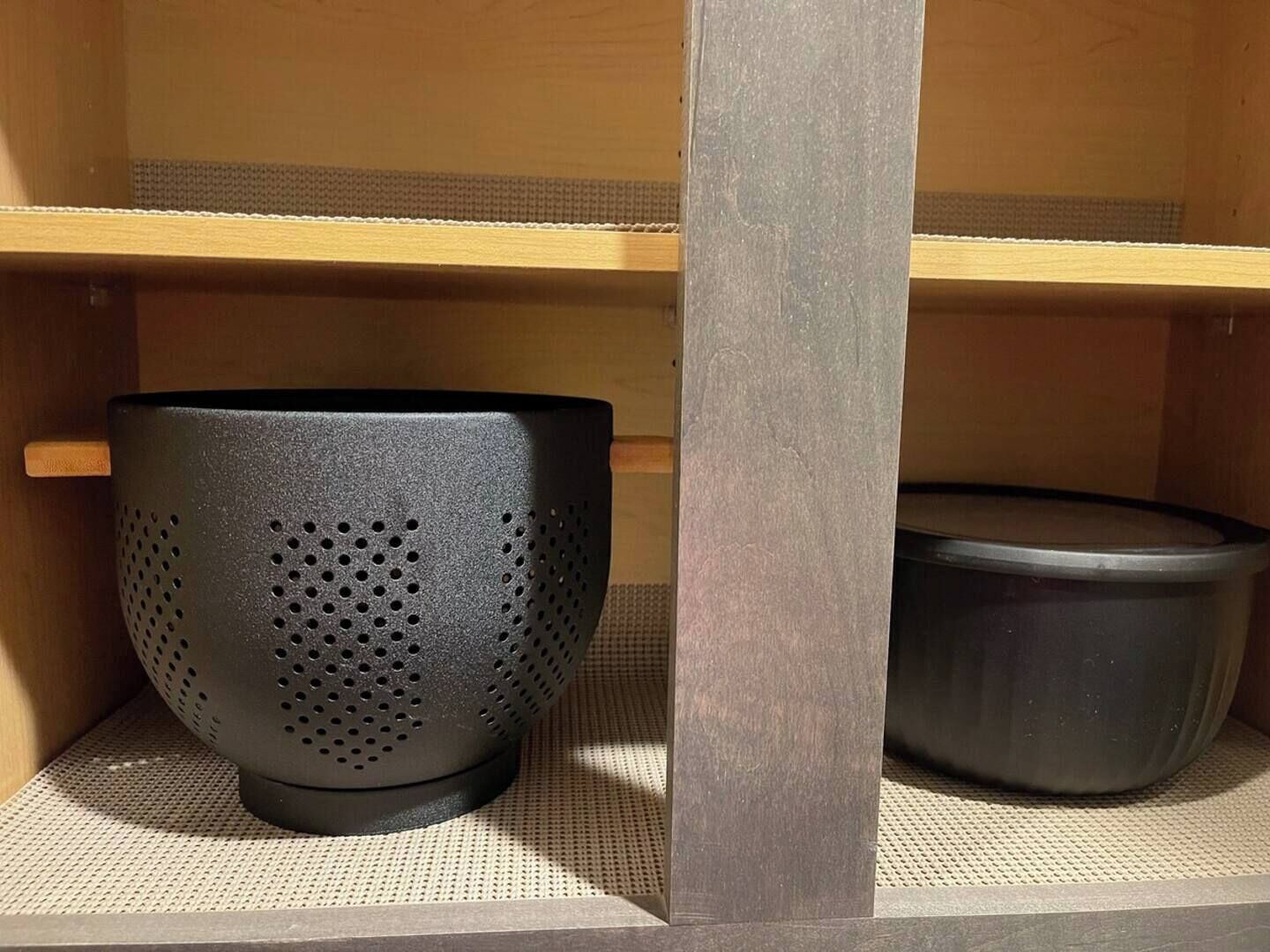 A shelf with a black perforated container and a black pot.
