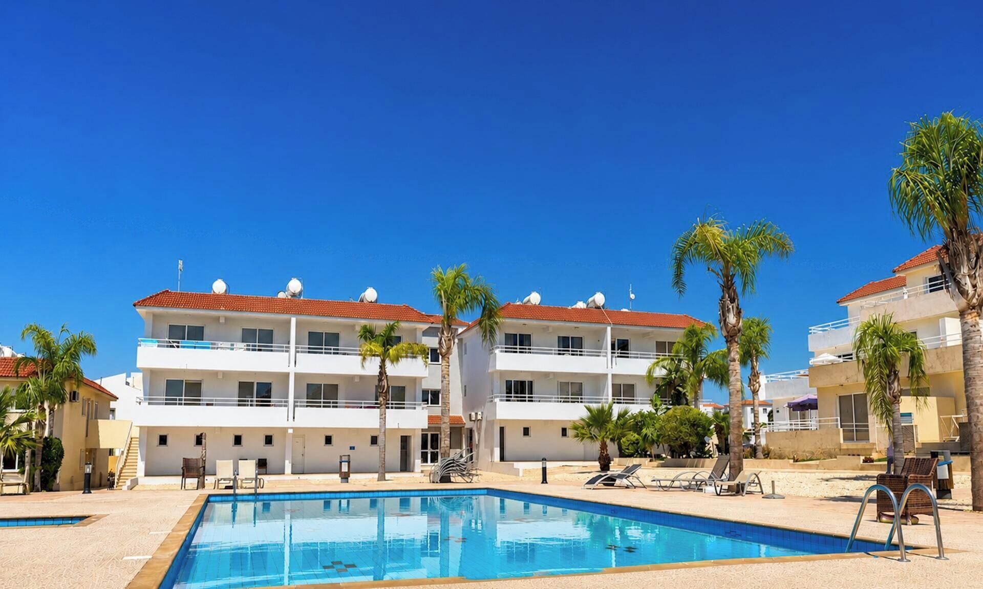 A hotel with a swimming pool, palm trees, and a clear blue sky.