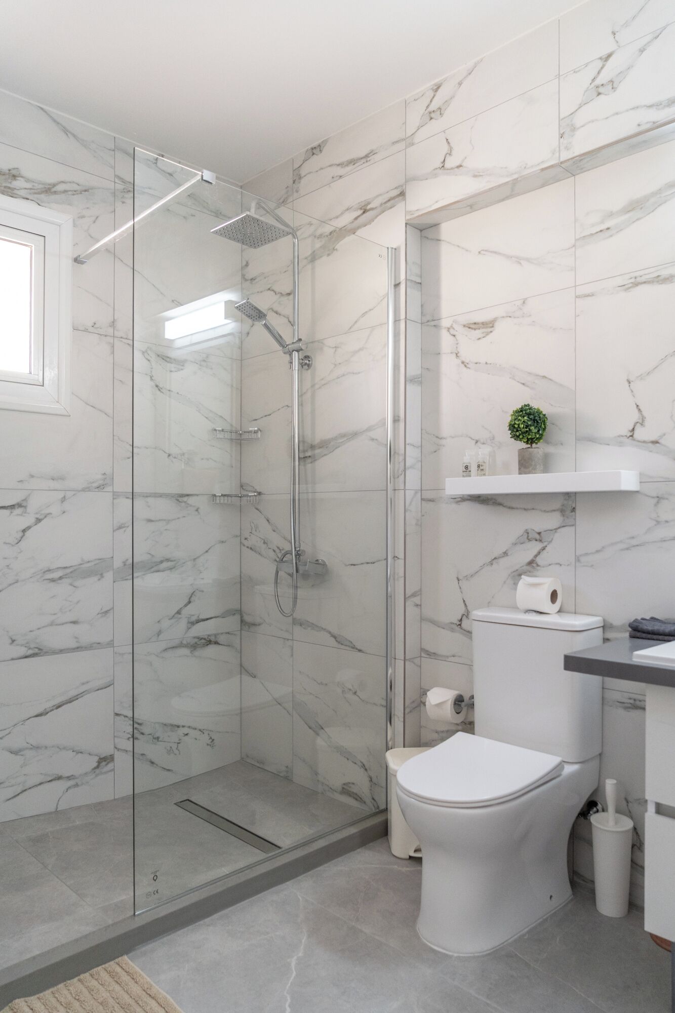 A modern bathroom with a glass-enclosed shower, a white toilet, and a marble-tiled wall.