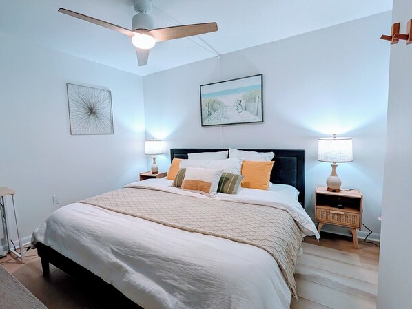 Un dormitorio con una cama, dos mesitas de noche, un ventilador de techo y cuadros en la pared.