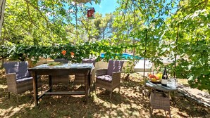 Un espace extérieur aménagé pour les repas, avec des meubles en osier, une table dressée avec des assiettes et une bouteille de vin.