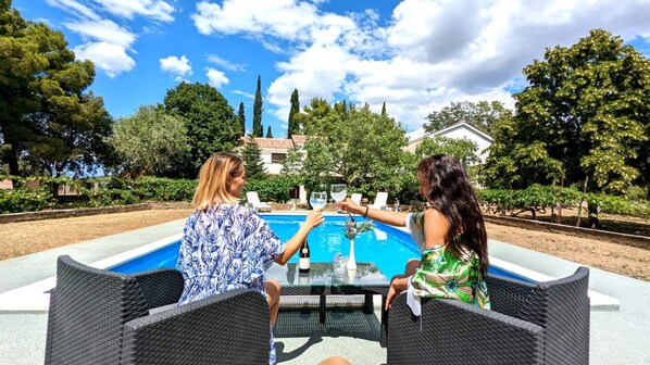 Two people sitting at a table by a pool with a clear sky and trees in the background. - Holiday Home Jaga (Polaca)