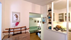 Un couloir avec un banc en bois, un tableau encadré représentant un hippocampe, et un lit en arrière-plan.