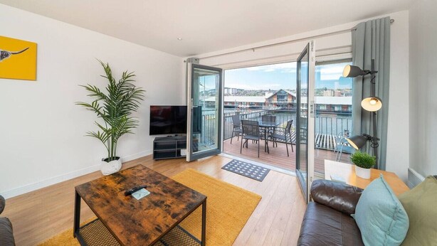 A modern living room with a television, a coffee table, a sofa, and a balcony with a view of the city. - Quayside Apartment - Central Location (Dundee)