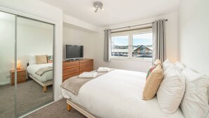 A bedroom with a bed, a TV, a dresser, and a window with a view of buildings. - Quayside Apartment - Central Location (Dundee)
