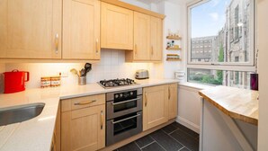 A compact kitchen with wooden cabinets, a gas stove, a toaster, and a window with a city view. - The Palais - Retro Style (Dundee)