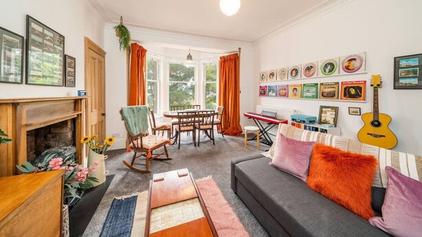 A cozy living room with a fireplace, a dining area, and a wall adorned with framed pictures. - The Palais - Retro Style (Dundee)