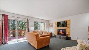 A living room with a fireplace, two sofas, a patterned armchair, and a balcony with red curtains. - Aspen- Spacious River Front, family cabin (Strawberry)