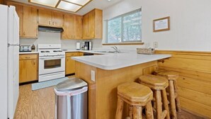 A kitchen with wooden cabinets, a white countertop, a stainless steel trash can, and wooden stools. - Aspen- Spacious River Front, family cabin (Strawberry)