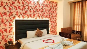 A hotel room with a bed, a nightstand, a chair, and a wall with floral wallpaper. - Grand Mostafa Hotel Ababil (Sylhet)