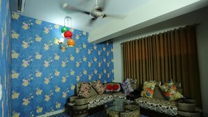 A living room with a sofa set, a glass coffee table, patterned wallpaper, and a ceiling fan. - Grand Mostafa Hotel Ababil (Sylhet)