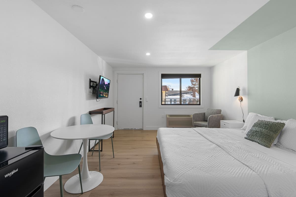 A modern hotel room with a bed, a desk, a chair, and a TV on the wall.