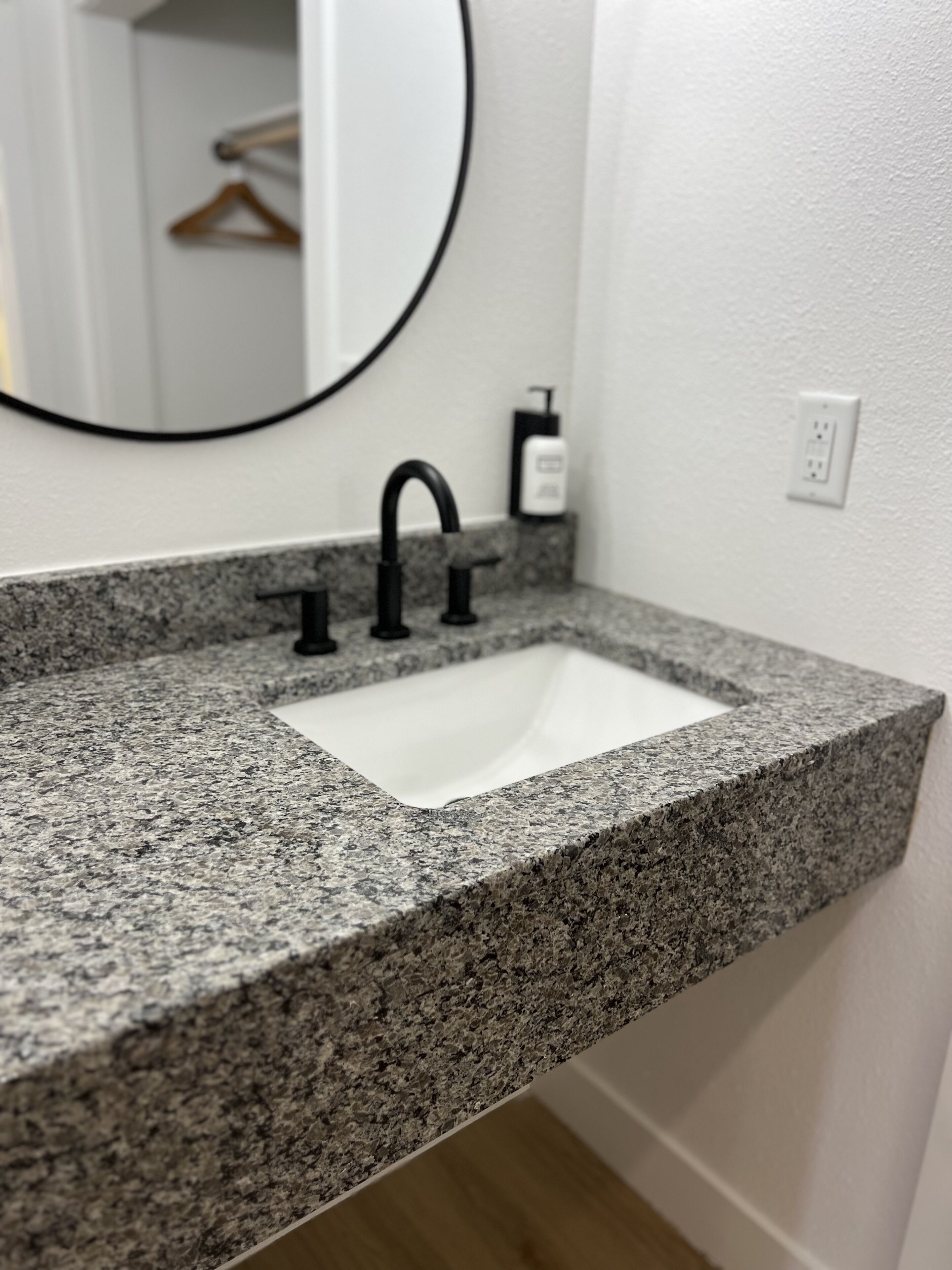 Un baño con encimera de granito, un lavamanos blanco y un grifo negro.
