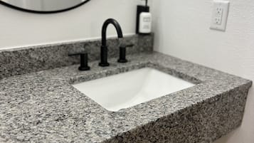 Ein Badezimmer mit einer Granit-Arbeitsfläche, einem weißen Waschbecken und einem schwarzen Wasserhahn.