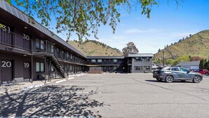 A modern building with numbered rooms, a parking area, and a view of a hilly landscape. - Cashmere Inn (Cashmere)