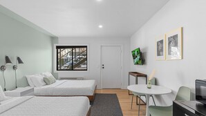 A modern hotel room with two beds, a desk, a chair, a TV, and a window with a view of a staircase. - Cashmere Inn (Cashmere)