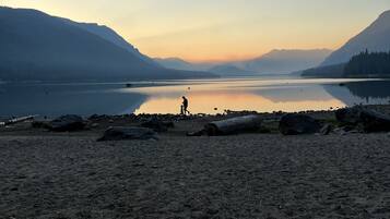A beach with a person walking, mountains in the background, and calm water.