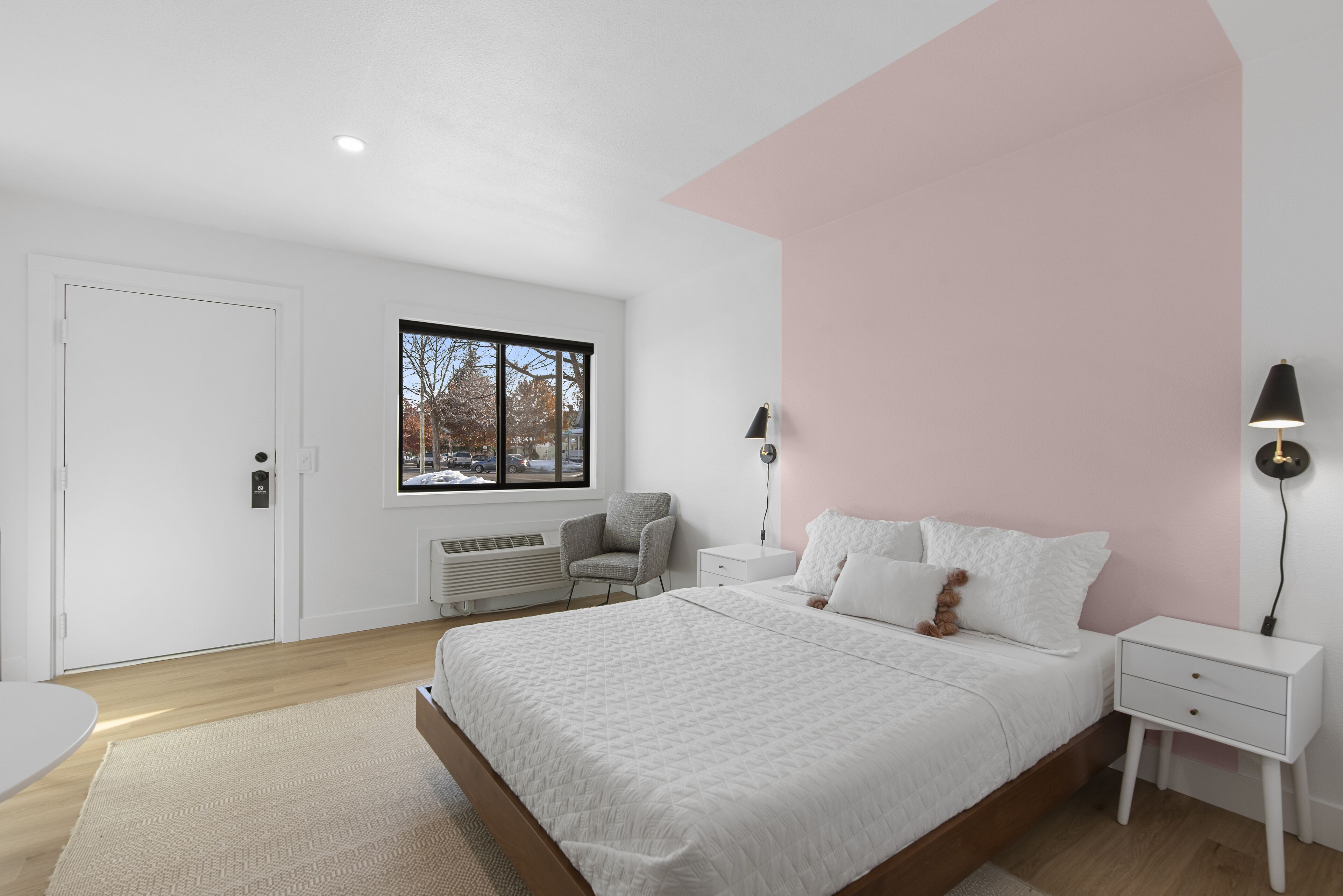 A bedroom with a large bed, a chair, a bedside table, a lamp, and a window with a view of trees.