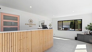 A reception area with a wooden reception desk, a large window with a view of a building and trees, and a sign that reads "CASHIER IN". - Cashmere Inn (Cashmere)