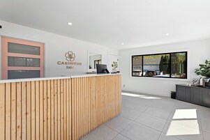 Un área de recepción con un mostrador de madera, un ventanal con vista a un edificio y árboles, y un cartel que dice