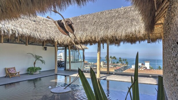 A pool area with a thatched roof, a view of the ocean, and a lounge chair. - Beautiful condo in the heart of Zona Romantica and steps to Los Muertos Beach! 1 (Puerto Vallarta)