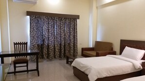 A hotel room with a bed, a desk, a chair, and a window with patterned curtains. - The Sravasti Residency (Ikauna)