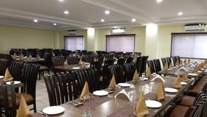 A conference room with multiple tables set for dining, equipped with chairs and tables, and air conditioning units on the walls. - The Sravasti Residency (Ikauna)