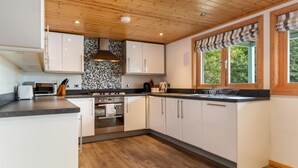 Une cuisine moderne avec des armoires blanches, un comptoir noir, un plafond en bois et une fenêtre agrémentée d’une lambrequin à rayures.