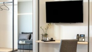 Un espace de bureau moderne avec un téléviseur à écran plat fixé au mur, un bureau avec un téléphone, une orchidée en pot et un canapé gris en arrière-plan.