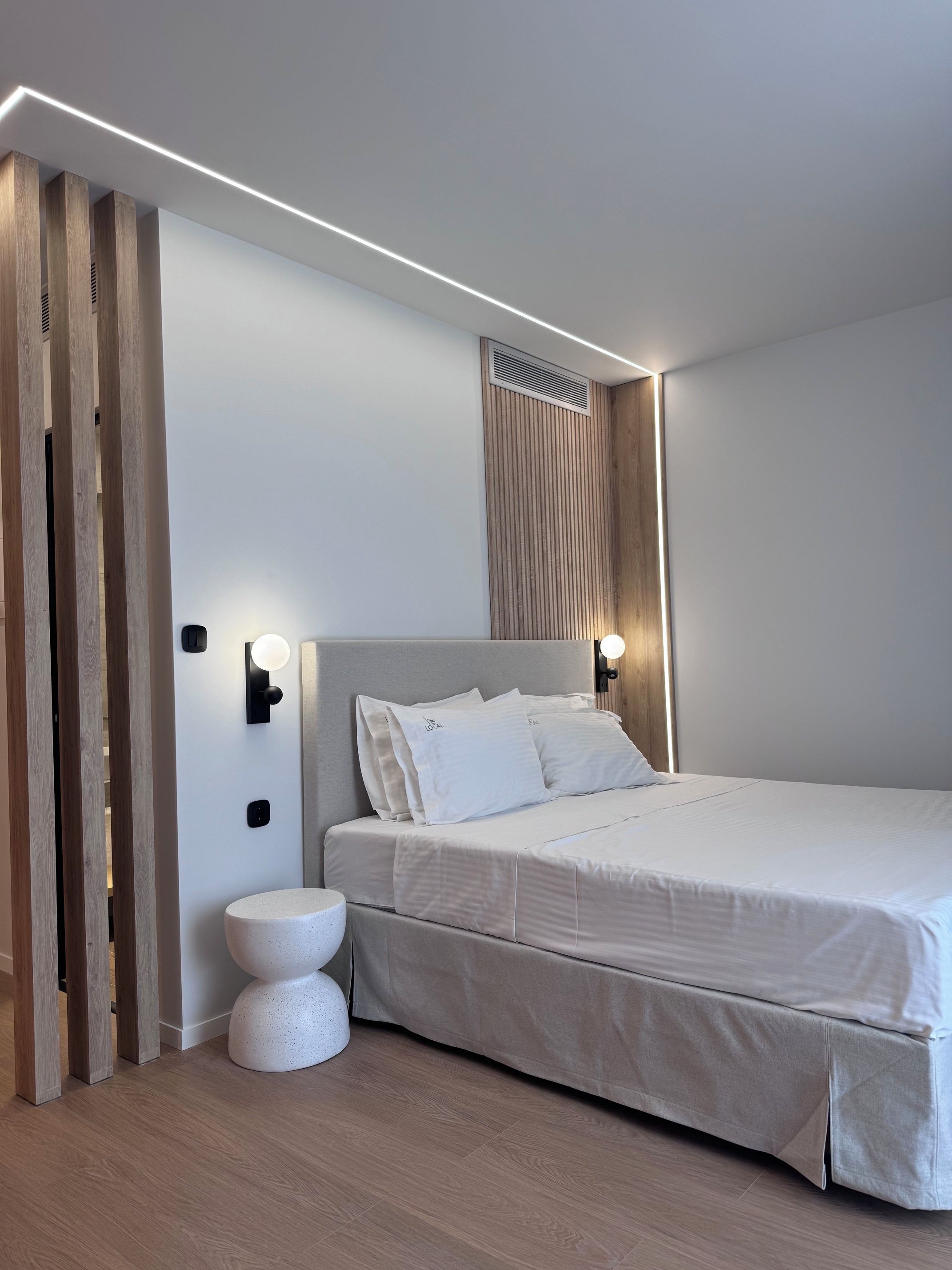A modern bedroom with a large bed, a round bedside table, and a wall-mounted light fixture.