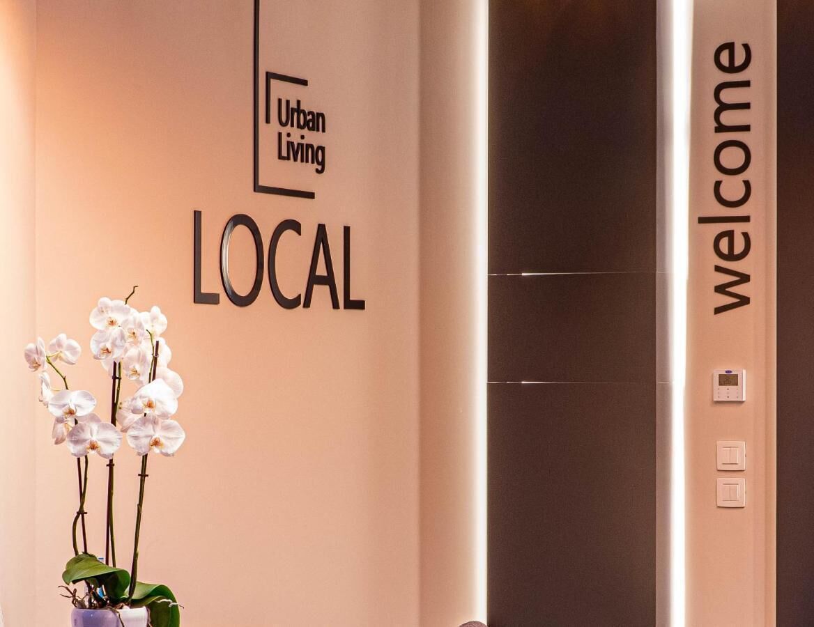 A reception area with a wall sign reading "Urban Living LOCAL" and a "welcome" sign above an elevator.