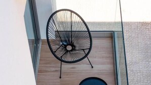 Ein moderner Balkon mit Glasgeländer, zwei schwarzen Metallstühlen und einem kleinen runden Tisch.