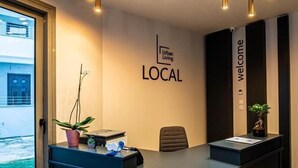 Ein Empfangsbereich mit modernem Design, mit einer schwarzen Theke, einer Zimmerpflanze und einem Schild mit der Aufschrift 'Urban Living LOCAL'.