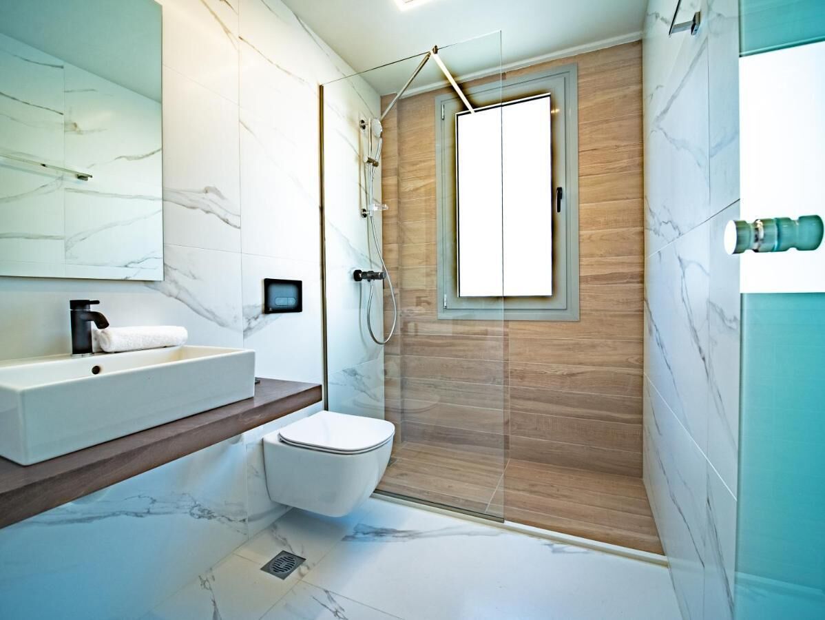 A modern bathroom with a marble vanity, a toilet, and a glass-enclosed shower area.