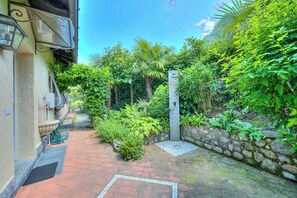 A narrow brick pathway leading to a stone wall with lush greenery and a small garden area.