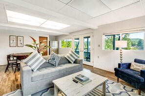 Sala de estar com sofá cinza, poltrona azul, mesa de centro e área de jantar com mesa e cadeiras.