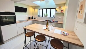 Une cuisine moderne équipée d’un four encastré, d’une machine à café et d’une bouteille de vin posée sur le plan de travail.