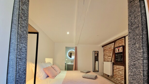 Une chambre d’hôtel moderne dotée d’un grand lit, d’un miroir, d’un mur décoratif en briques et d’un panneau indiquant qu’il n’est pas nécessaire de présenter une carte de crédit.