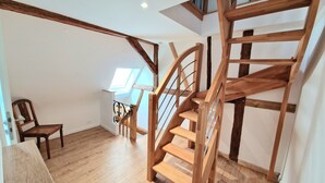 Un escalier en bois avec un puits de lumière, une chaise en bois et une table en bois dans une pièce aux murs blancs et au plancher en bois.