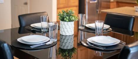 Enjoy meals in this dining area with a polished table set for four, featuring a vase with a small plant and modern kitchen in the background.
