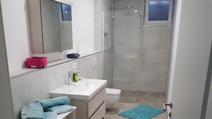 Un baño moderno con lavamanos, inodoro y ducha. Hay un espejo sobre el lavamanos y una pequeña ventana sobre la ducha.
