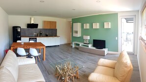 Una sala de estar moderna con un sofá, una mesa de centro y un televisor. Hay una zona de cocina con armarios y un microondas.