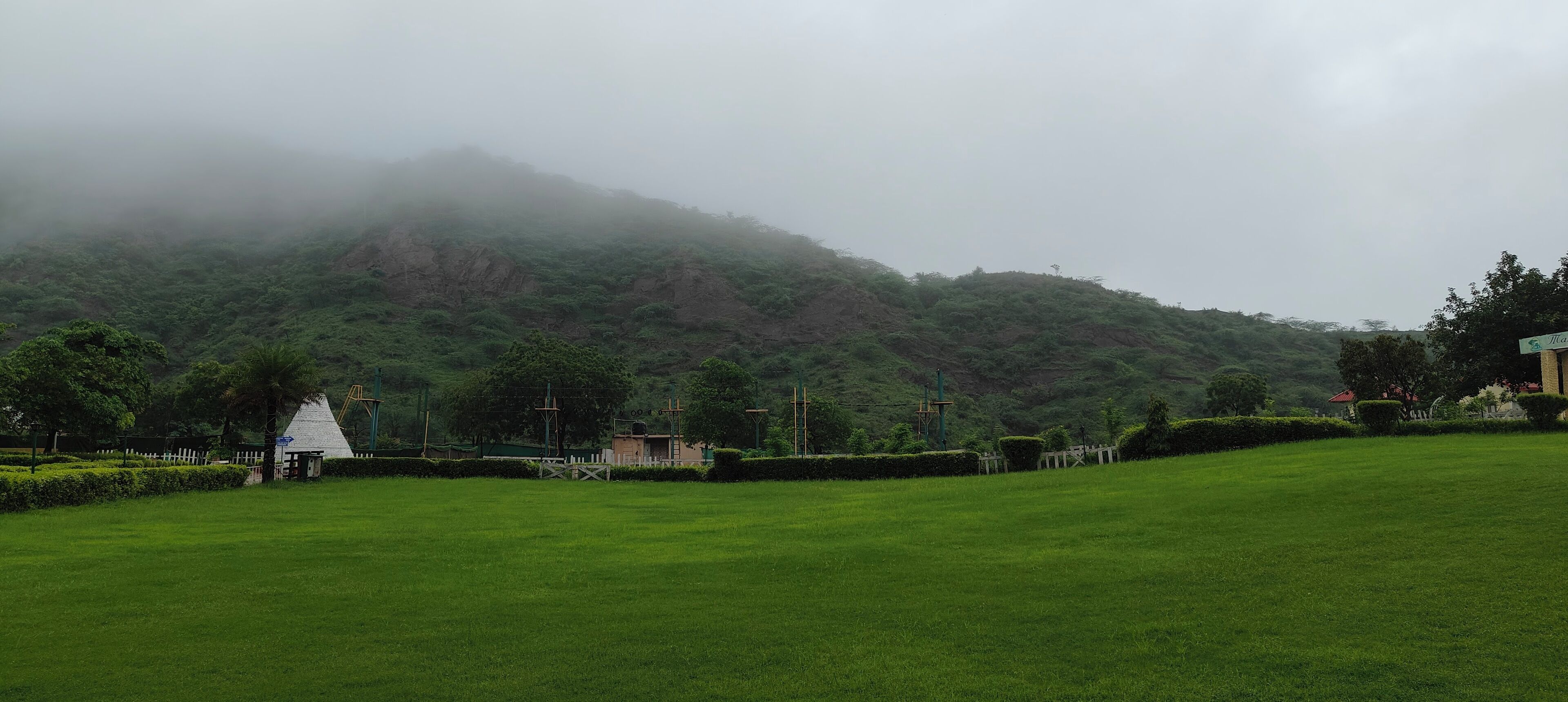 A grassy field with a white building and a hill in the background.