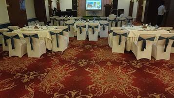 A banquet hall with round tables, chairs with blue sashes, a red carpet, and a projection screen in the background.