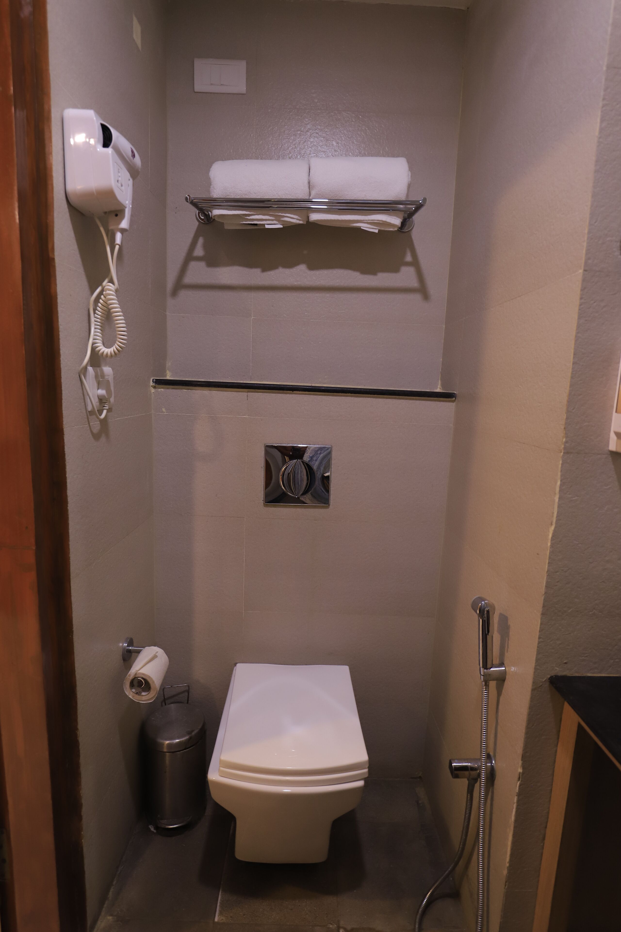 Un bagno compatto con il water, un asciugatore di mani, un cestino e un porta asciugamani.