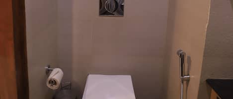 Un bagno compatto con il water, un asciugatore di mani, un cestino e un porta asciugamani.