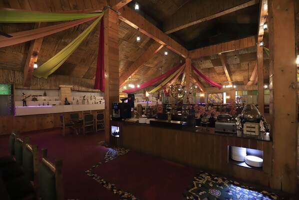 A rustic wooden interior with a high ceiling, a bar area, and a seating area with chairs. - MANOHAR VILLAS (Neemrana)