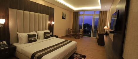 A hotel room with a large bed, a flat-screen TV, a desk, and a balcony with a city view.