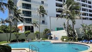 Ein Swimmingpool mit Liegestühlen und Palmen, umgeben von einem Gebäude mit Balkonen.